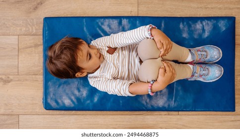 Adorable young girl enjoying in her physical therapy sessions, playing contentedly in a children's gym designed for therapeutic activities. She happy and lies on an exercise mat. View from above. - Powered by Shutterstock