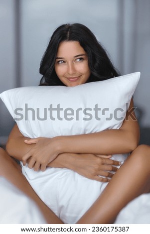 Adorable young happy woman hugging pillow on comfortable bed with silky linens. High quality photo for promotion or online shop advertisement 