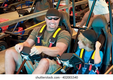 Adorable Young Kid  With His Dad On A Go Cart At An Amusement Park.