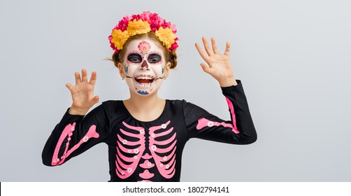 Adorable Zombie In Flower Wreath Posing On Grey Background. Happy Child With Halloween Creative Makeup. Girl Celebrating For Mexican Day Of The Dead.