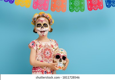 Adorable Zombie In Flower Wreath Posing On Blue Background. Happy Child With Halloween Creative Makeup. Girl Celebrating For Mexican Day Of The Dead.