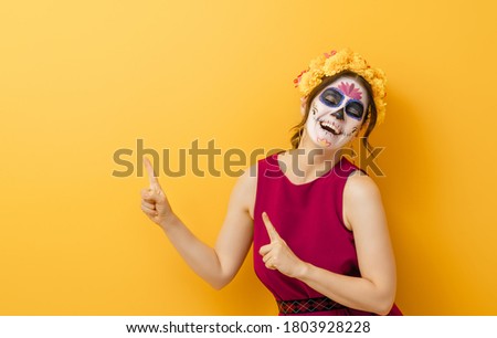 Adorable zombie in flower wreath posing on yellow background. Happy woman with Halloween creative makeup. Girl celebrating for Mexican Day of the Dead.