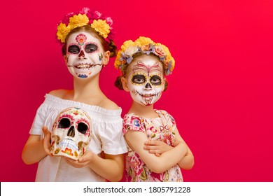 Adorable zombies in flower wreaths posing on red background. Happy children with Halloween creative makeup. Girls celebrating for Mexican Day of the Dead.