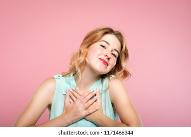 adoration and tender emotion. pretty blond girl smiling and pressing both hands to her heart. sweet reaction and pleasant feelings concept. young beautiful woman on pink background. - Shutterstock ID 1171466344
