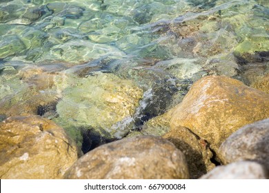 Adriatic sea water waves rolling on rocks at the beach.Crystal clear water with transparent surface shine under the bright summer sun at exotic tropical resort.Ocean tidal wave at seaside