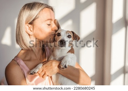 Adult 40s woman with her cute dog Jack Russell Terrier in armchair at home. Lovely pet
