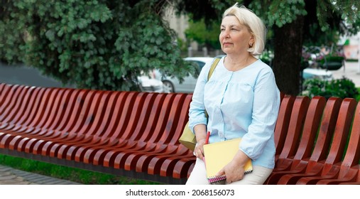 Adult 50 Years Old Teacher Woman On A Wooden Bench In A Park Holding Books