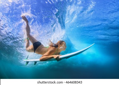 Adult active girl in bikini in action - surfer with surf board dive underwater under breaking big ocean wave. Family lifestyle, people water sport adventure camp, beach extreme swim on summer vacation