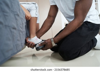 Adult African American Man Putting Shoes On Foot Of Child