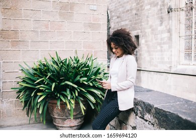 Adult African American Pleased Tourist In Casual Clothes Focusing On Screen And Interacting With Smartphone On Street Near Old Stone Building In Gothic Style In Barcelona