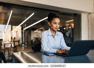 Adult African woman sitting at the office and typing something on the laptop. - Powered by Shutterstock