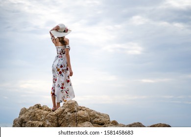 Adult asia woman travel to the sea and standing relax on the rock looking to sky. Hand holding the hat in dress cloth with rear view. Pattaya, Thailand.