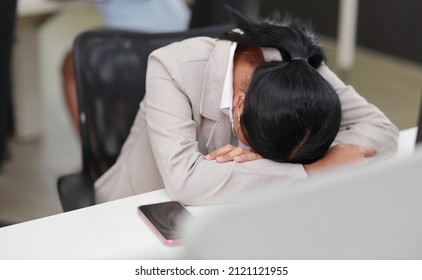 Adult asian businesswoman sitting and lying face down on table with smart mobile phone after bad news business failure or get fired and feeling discouraged, distraught and hopeless in modern office