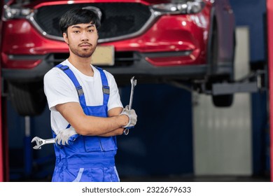 Adult Asian handsome male mechanic wearing uniform, crossed arms, posing with confidence, standing in garage at car or automobile maintenance service center or shop with copy space. Industry Concept - Shutterstock ID 2322679633