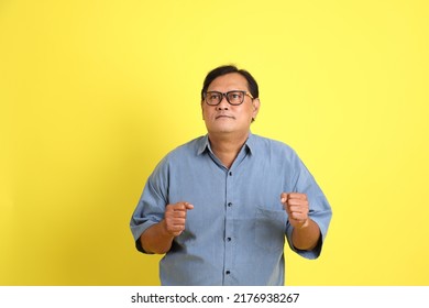 The Adult Asian Man With Blue Shirt Standing On The Yellow Background.