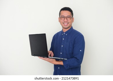 Adult Asian Man Looking To The Camera While Holding A Laptop And Showing Happy Expression