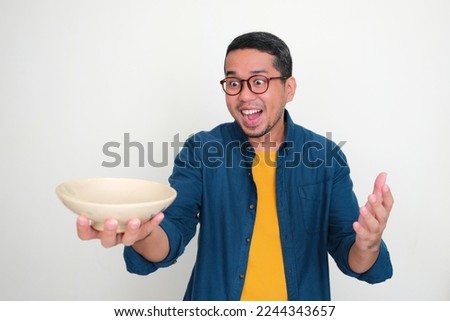 Adult Asian man looking at empty bowl that he hold with excited expression