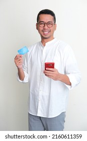 Adult Asian Man Looking And Smiling To Camera While Holding Mobile Phone And Credit Card 