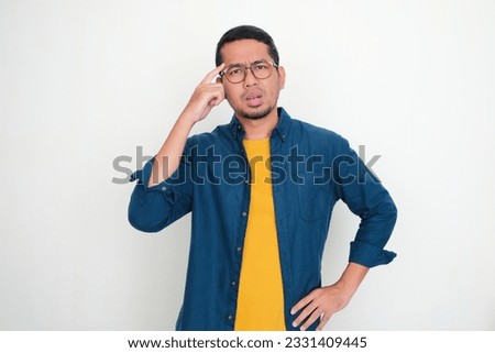 Adult Asian man pointing to his temple with confuse expression