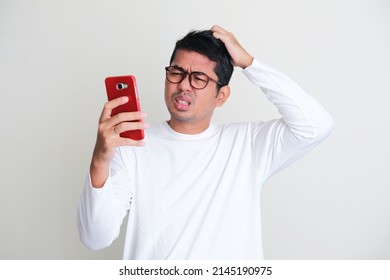 Adult Asian Man Scratching His Head And Showing Confused Expression While Looking To His Mobile Phone