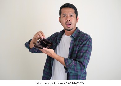 Adult Asian man showing empty wallet with shocked face expression