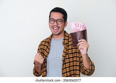 Adult Asian man showing excited face expression while holding his wallet full of money - Shutterstock ID 2065062077