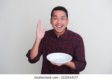 Adult Asian man showing excited expression while holding empty dinner plate