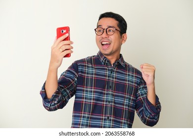 Adult Asian Man Showing Happy Gesture While Looking To His Mobile Phone