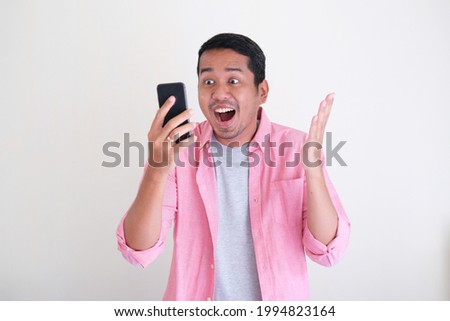 Adult Asian man showing happy face expression while looking to the mobile phone screen