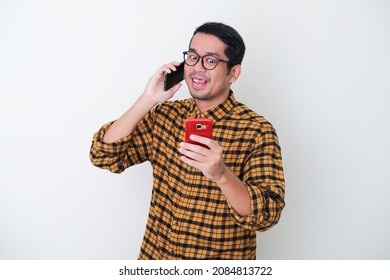 Adult Asian man showing mischievous face when caling someone and sending message to other at the same time