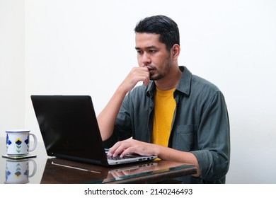 Adult Asian Man Showing Thinking Gesture  In Front Of His Laptop