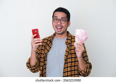 Adult Asian Man Showing Wow Face Expression While Holding Mobile Phone And Paper Money