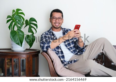 Adult Asian man sitting relax in a couch while holding mobile phone
