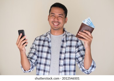 Adult Asian Man Smiling Happy While Holding Mobile Phone And Showing Paper Money From His Wallet