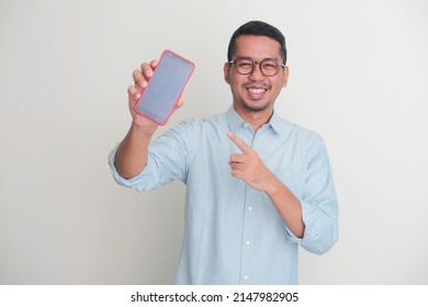 Adult Asian Man Smiling Happy While Showing Blank Mobile Phone Screen And Pointing On It