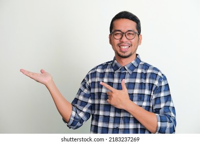 Adult Asian man smiling with left hand pointing to his opened right hand palm - Shutterstock ID 2183237269