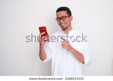 Adult Asian man smiling when looking to his mobile phone and pointing at it