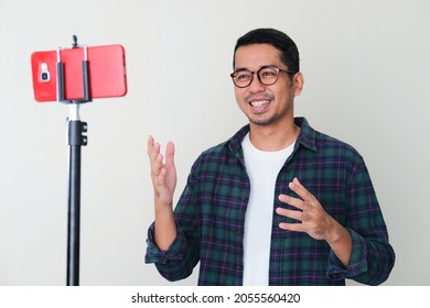 Adult Asian man smiling while presenting something using mobile phone call conference