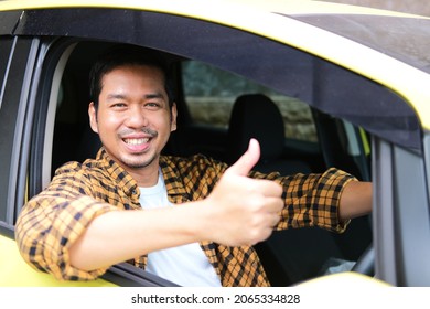 Adult Asian man smiling while giving thumb up from inside his car driver seat