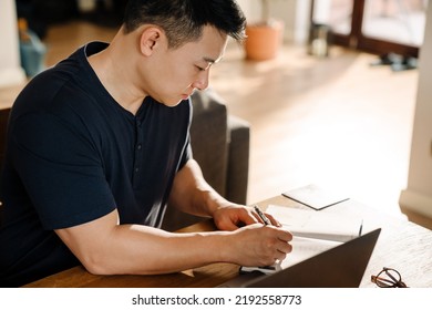 Adult Asian Man Taking Notes While Studying Working At Home