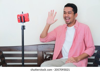 Adult Asian Man Waving Hand With Happy Face Expression During Video Call 