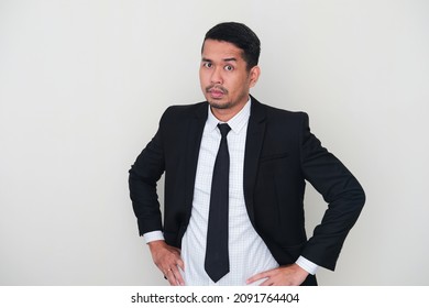 Adult Asian man wearing black suit and tie showing fierce face with his hands on hip