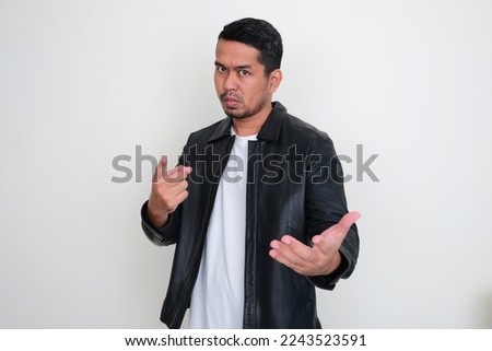 Adult Asian man wearing black leather jacket showing cruel expression while asking something forcefully