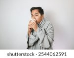 Adult Asian man wearing blanket and holding warm drink when got flu