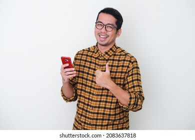 Adult Asian man wearing yellow flannel shirt smiling and give thumb up while holding mobile phone