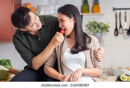 Adult Asian sweet lovely married couple wearing casual clothes, eating, feeding healthy strawberry fruit, smiling with love and happiness, standing in kitchen at cozy home. Lifestyle, Food Concept - Powered by Shutterstock