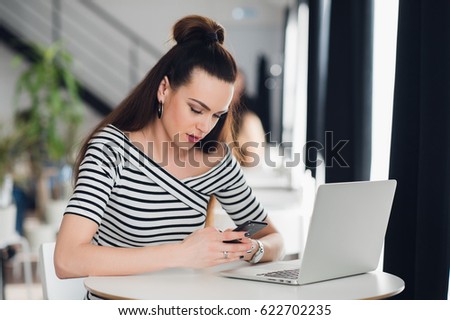 Adult attractive sleepy woman on her work holding phone and sitting with a laptop. Beautiful female napping on the job.