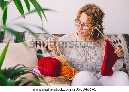 Adult attractive woman at home in knitting work activity using colorful wool. Happy and relaxed female people enjoying time indoor on the sofa. Knit job