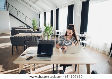 Adult attractive woman on her work is holding phone and sitting with a laptop. Beautiful female multitasking.