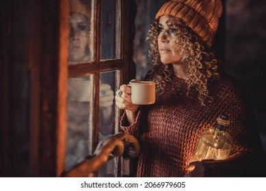 Adult attractive woman portrait standing at home and looking outside the windows with thoughts. Holiday winter atmosphere and light. Pretty serious expression female people